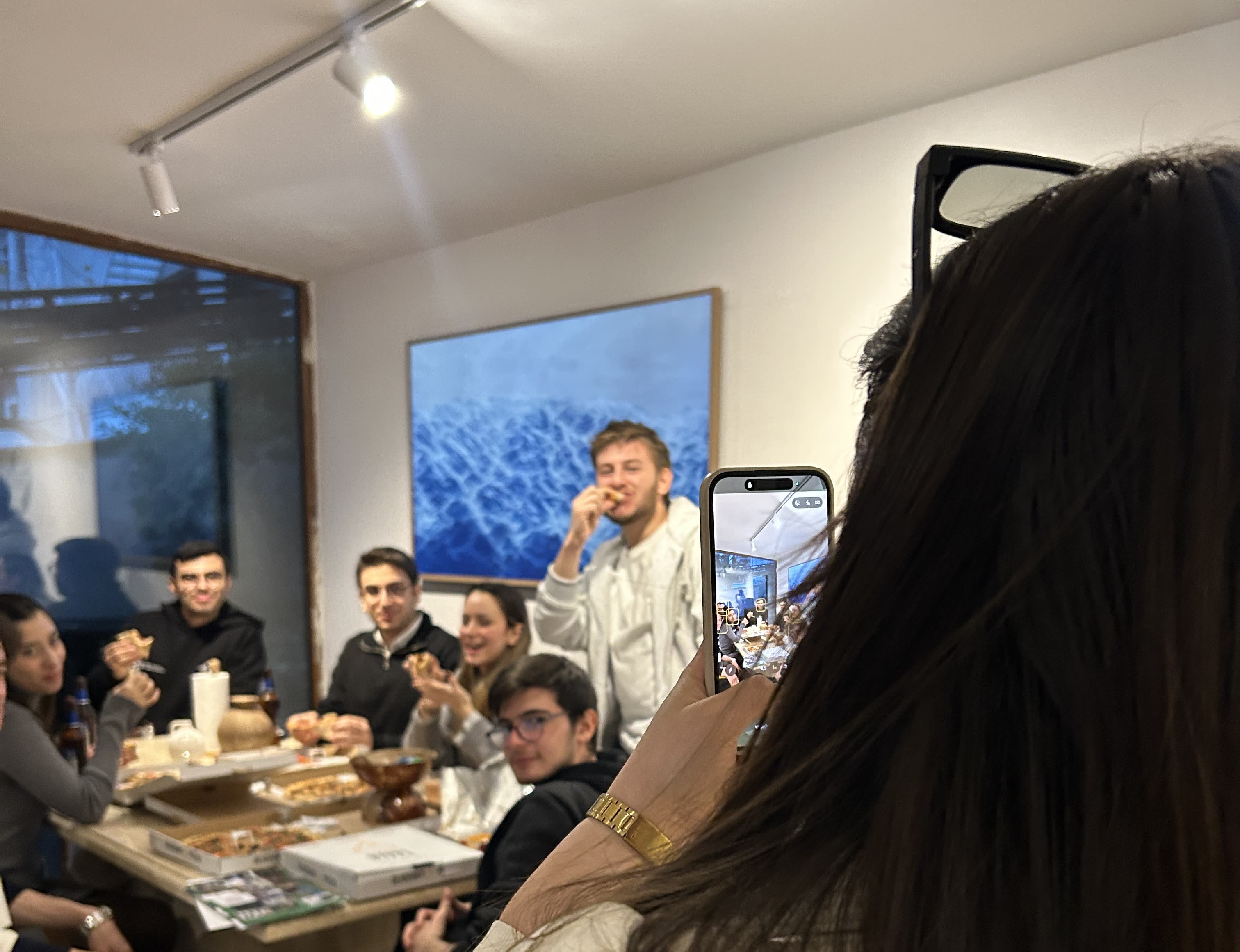 Tera Map Türkiye İstanbul etkinlik eventi Foligno Italia Tera Holding — Tera Holding Istanbul office pizza team event photo showing young professionals gathered around a wooden table with pizza boxes under blue wall art capturing a casual Tera Map Türkiye İstanbul etkinlik momenti